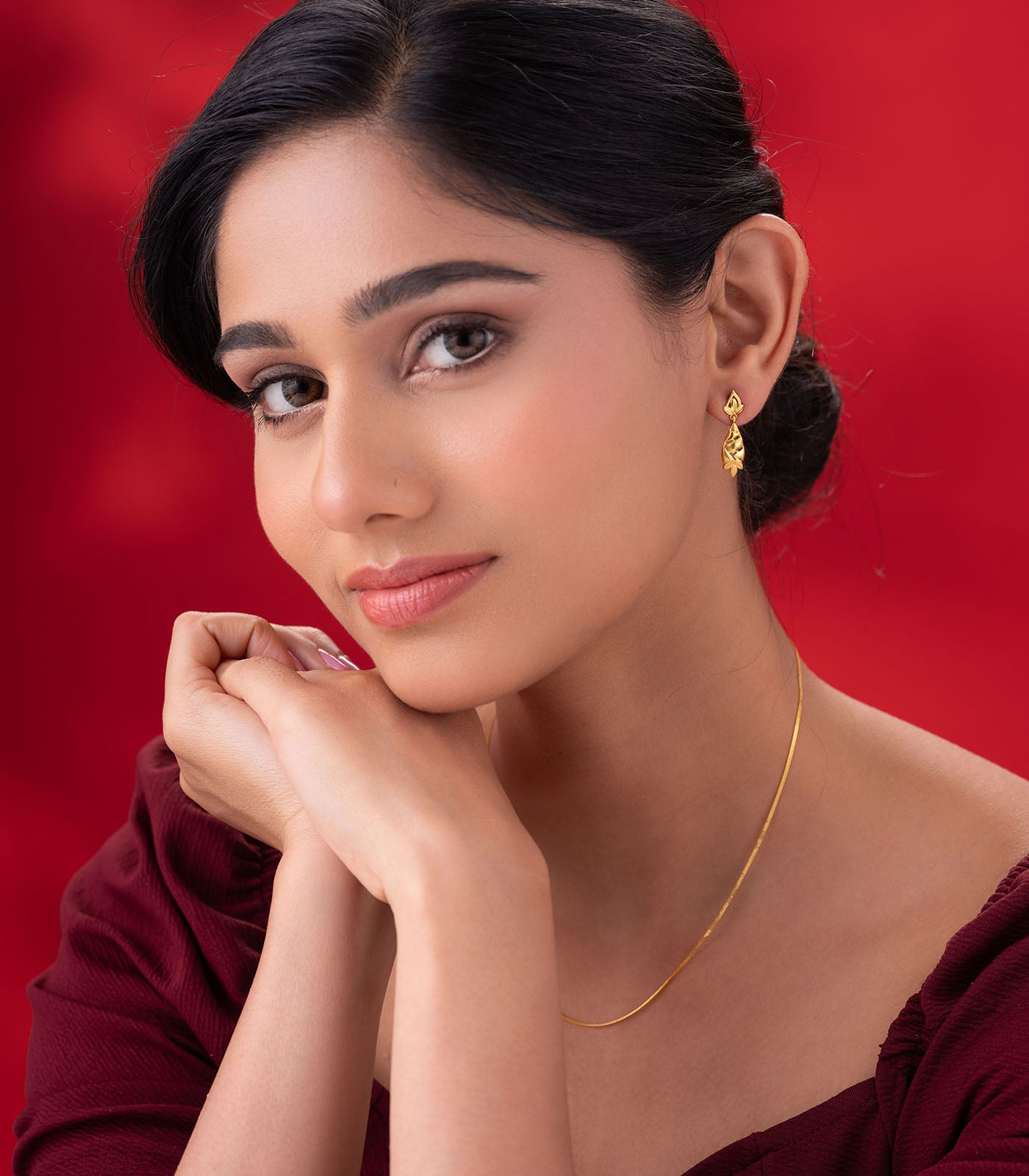 Woman wearing gold earring against a red background