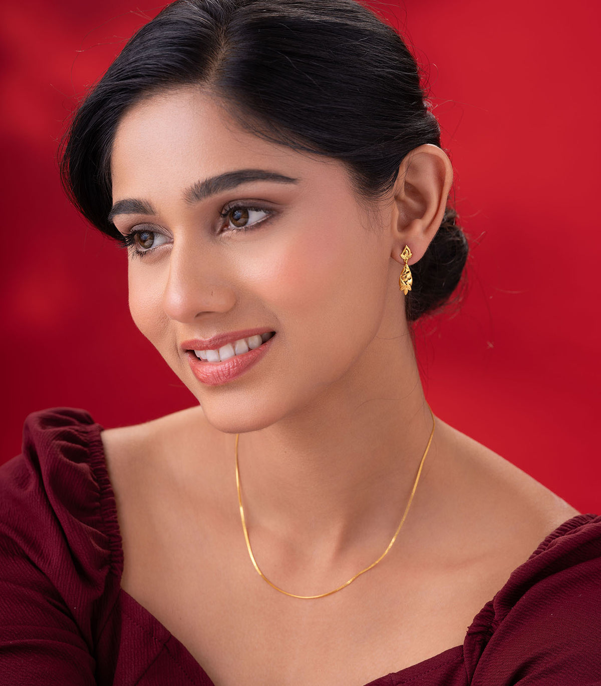 Woman wearing gold earring against a red background