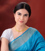 Woman wearing a blue saree with a gold necklace against a red background