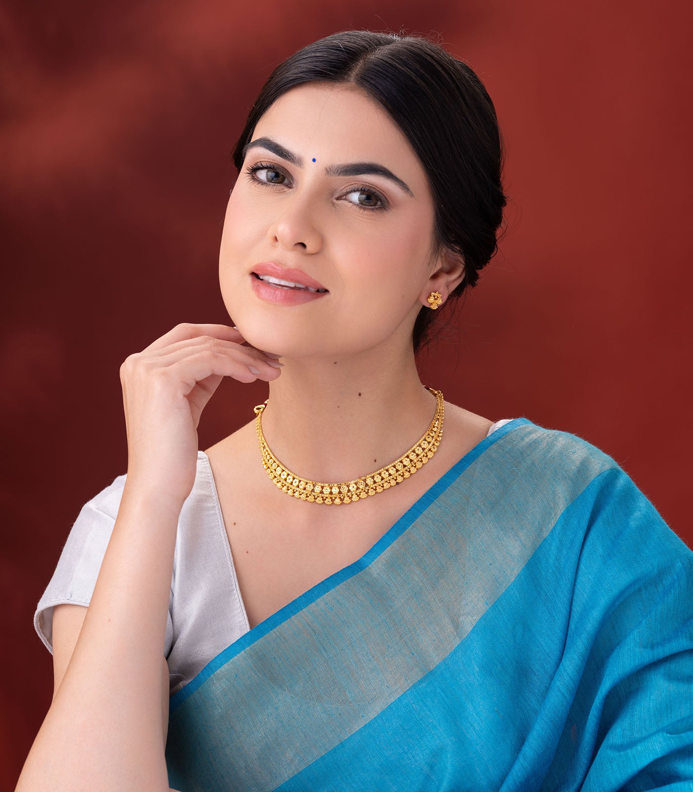 Woman wearing a blue saree with a gold necklace against a red background