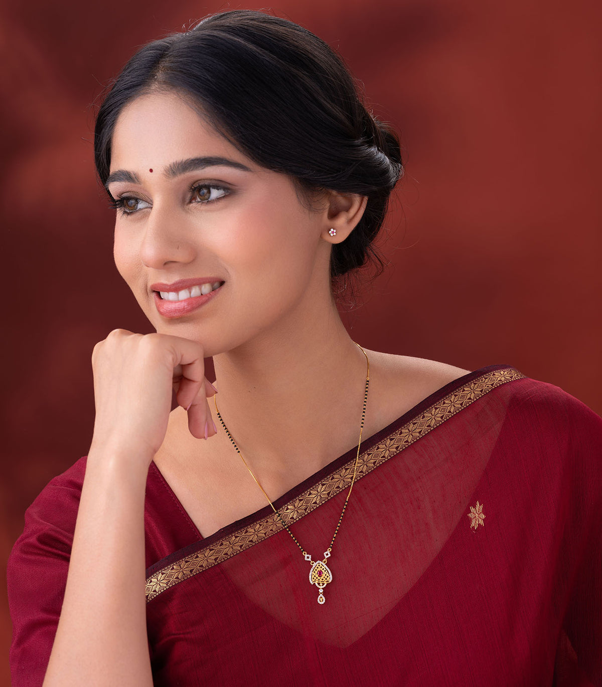 Woman wearing a delicate mangalsutra with a heart-shaped pendant on a red background