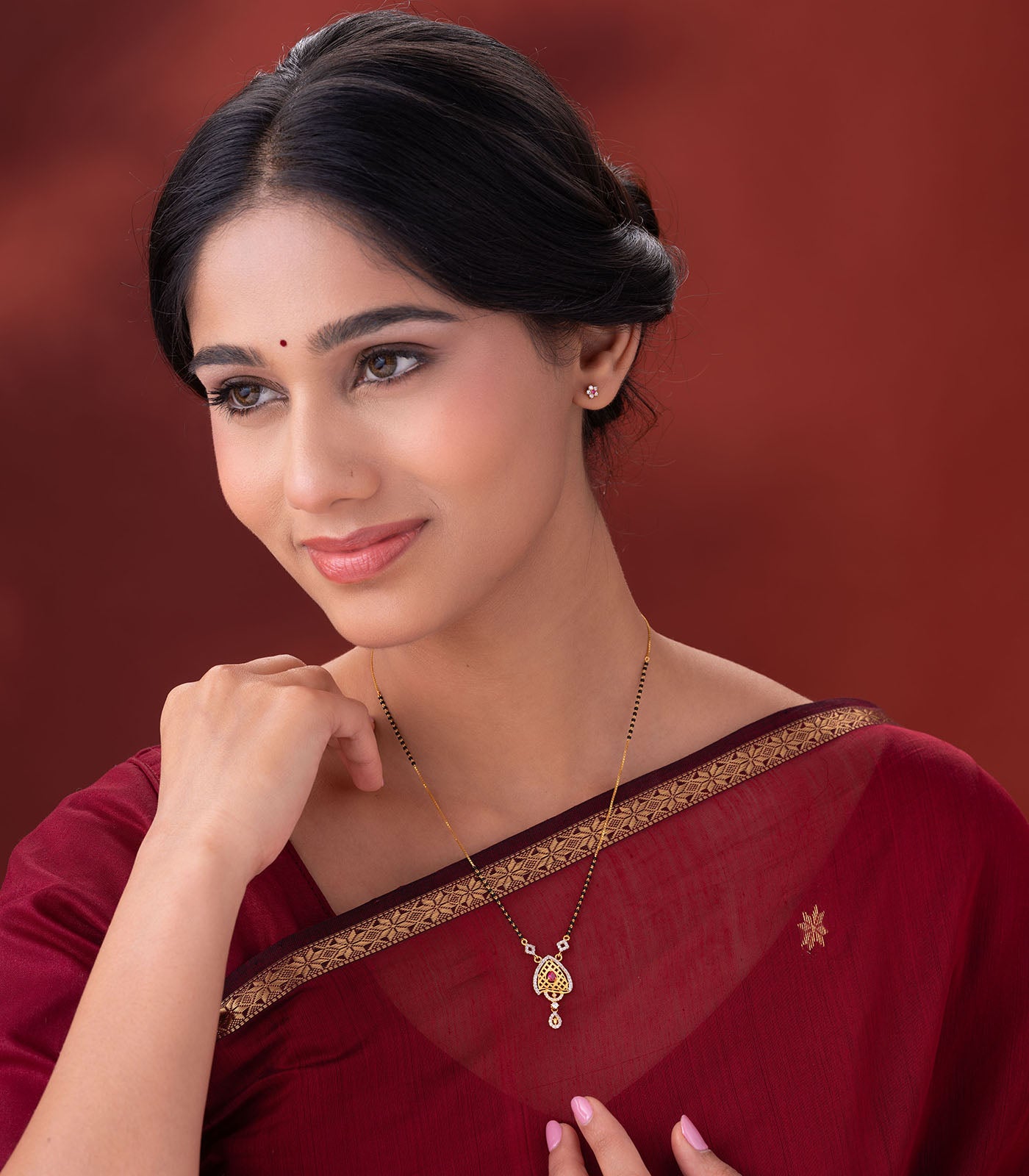 Woman wearing a delicate mangalsutra with a heart-shaped pendant on a red background