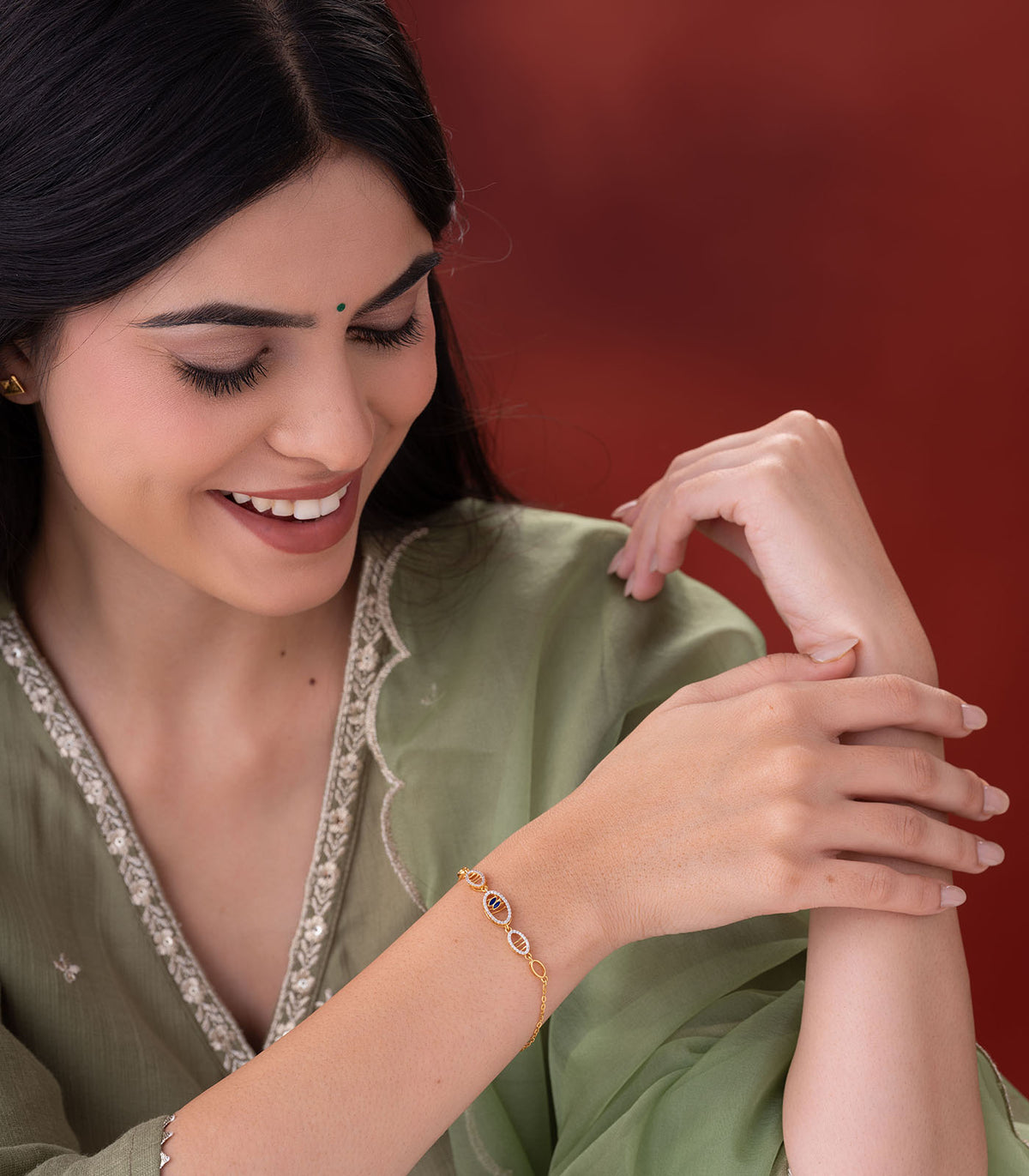 Woman wearing a gold bracelet on her wrist against a red background