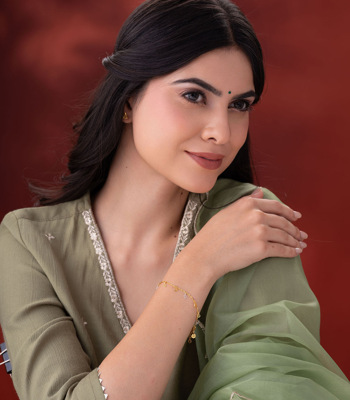 A woman wearing gold bracelet with geometric charms on a red background