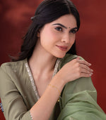 A woman wearing gold bracelet with geometric charms on a red background