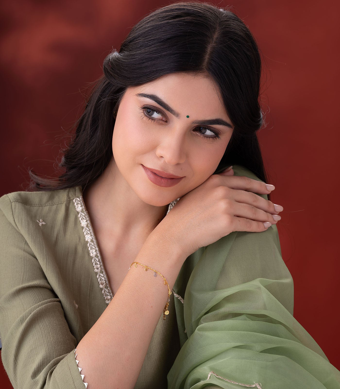 A woman wearing gold bracelet with geometric charms on a red background