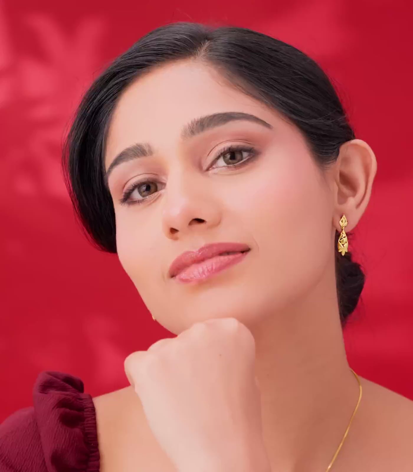 Woman flaunting gold earring against a red background