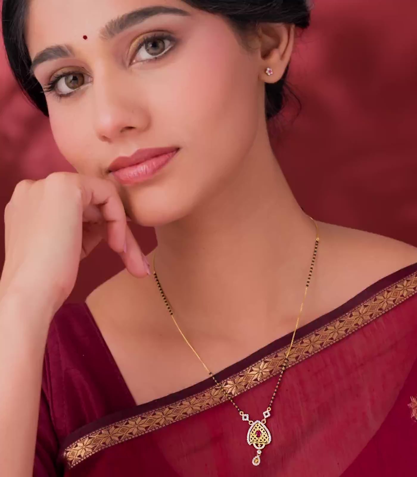 A woman flaunting delicate mangalsutra with a heart-shaped pendant on a red background